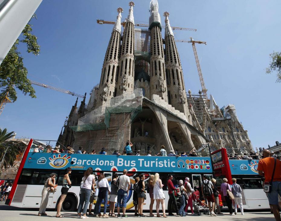 People queue up at a city tour bus stop in front of the Basilica Sagrada Familia in Barcelona