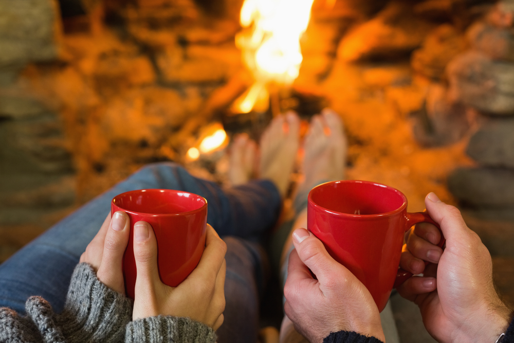 Close-up of hands holding red coffee cups in front of lit fireplace