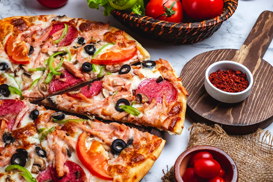 side-view-pizza-with-salami-ham-green-peppers-tomatoes-black-olives-cheese-table_141793-2996