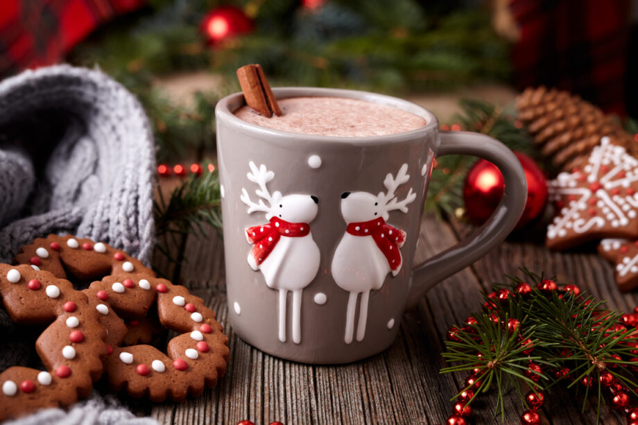 Cup of hot chocolate or cocoa beverage with two cute deer, cinnamon and gingerbread round christmas cookies in new year tree decorations frame on vintage wooden table background. Homemade traditional celebration recipe.